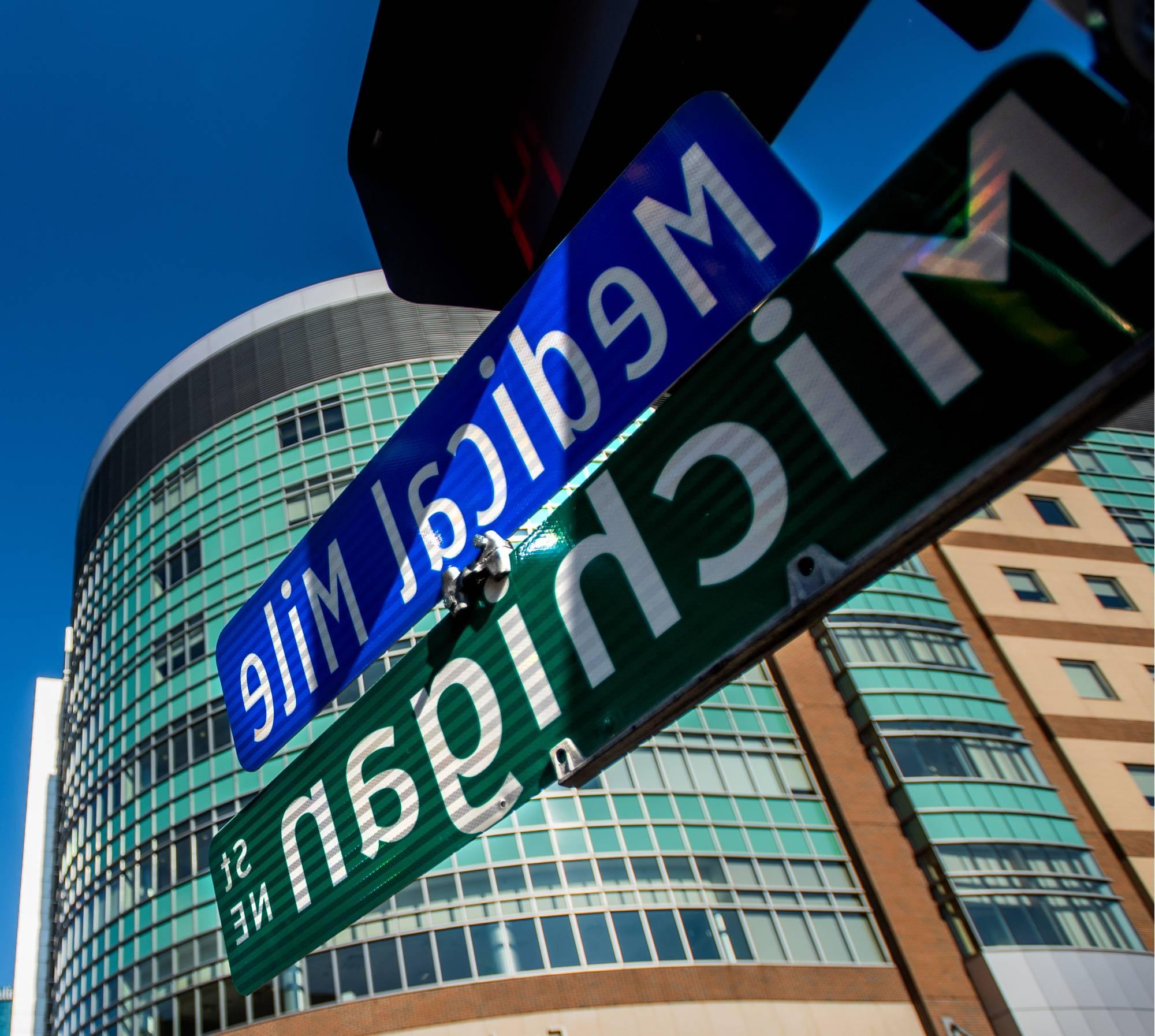 Close up photo street signs listing "密歇根 Street NE" and "Medical Mile", with a medical building in the distance.